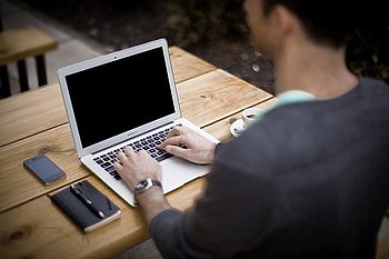 Eine Person sitzt an einem Laptop, neben sich ein Notizbuch und ein Mobiltelefon.